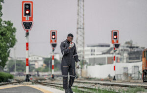 A railway signal maintainer communicates via radio while walking along the tracks, ensuring safety and coordination. The critical role of maintenance in the efficient operation of the railway system.